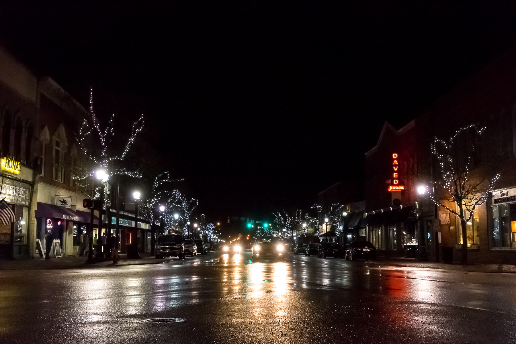Downtown Willoughby Ohio at night, wet streets reflecting Christmas lights, neon signs