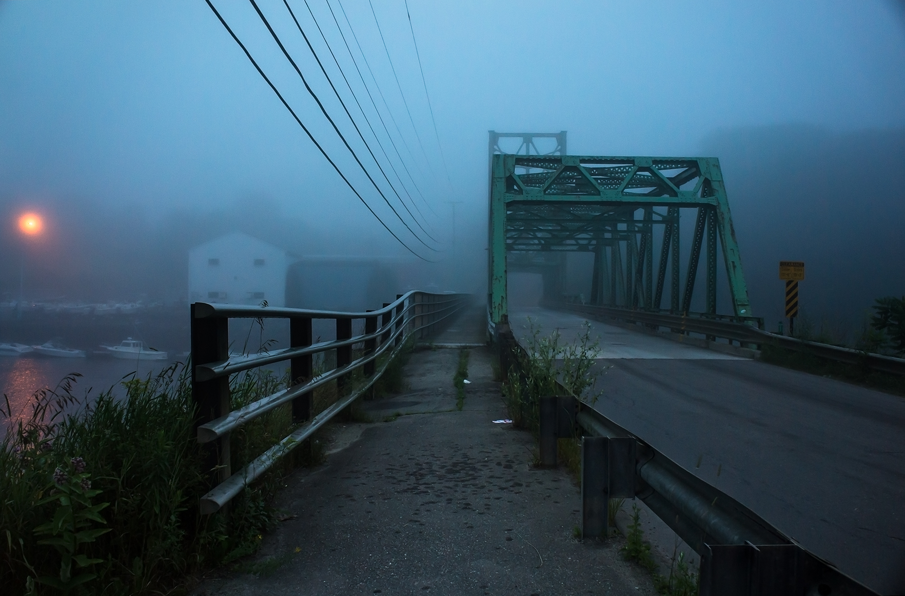 Old green iron bridge disappearing into dense coastal fog at dawn, Maine harbor