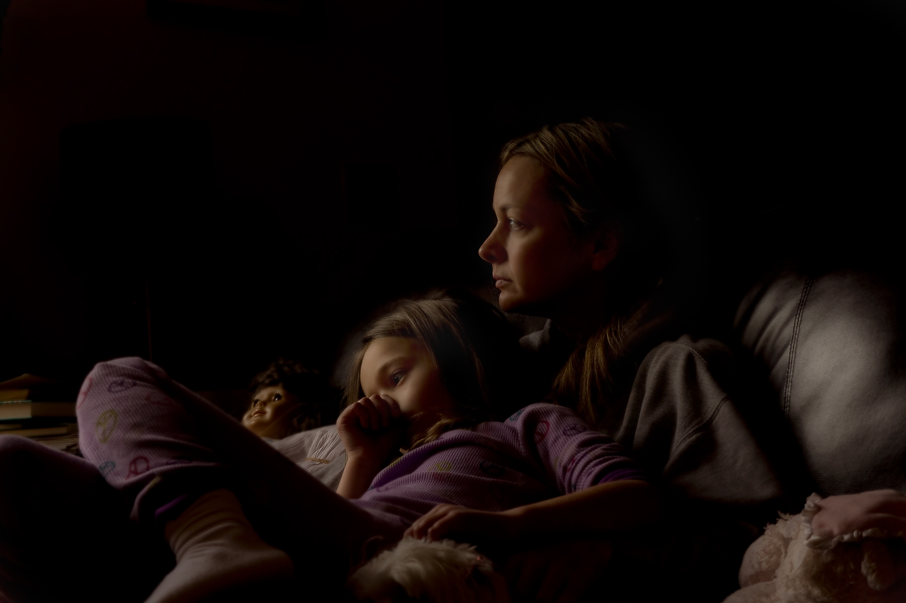 Mother and child lit by screen glow in darkness, intimate available light portrait